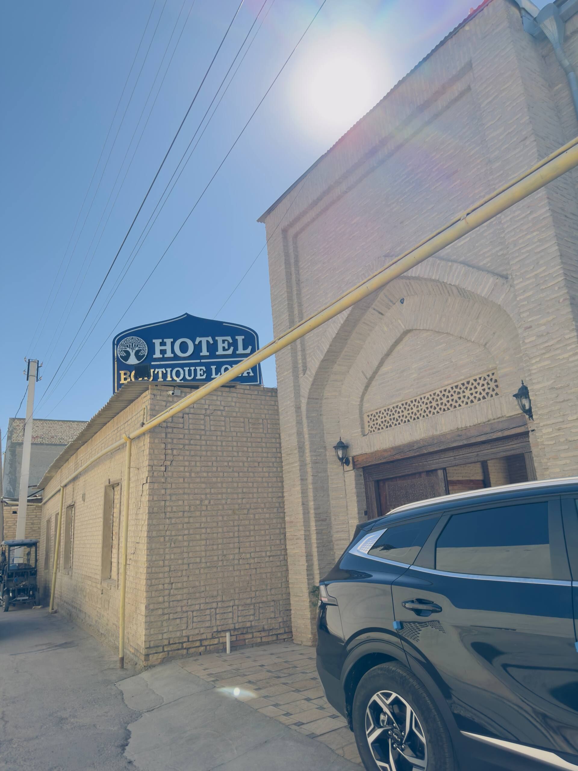 Letrero de hotel con logotipo de árbol, edificio de ladrillo y un coche estacionado.