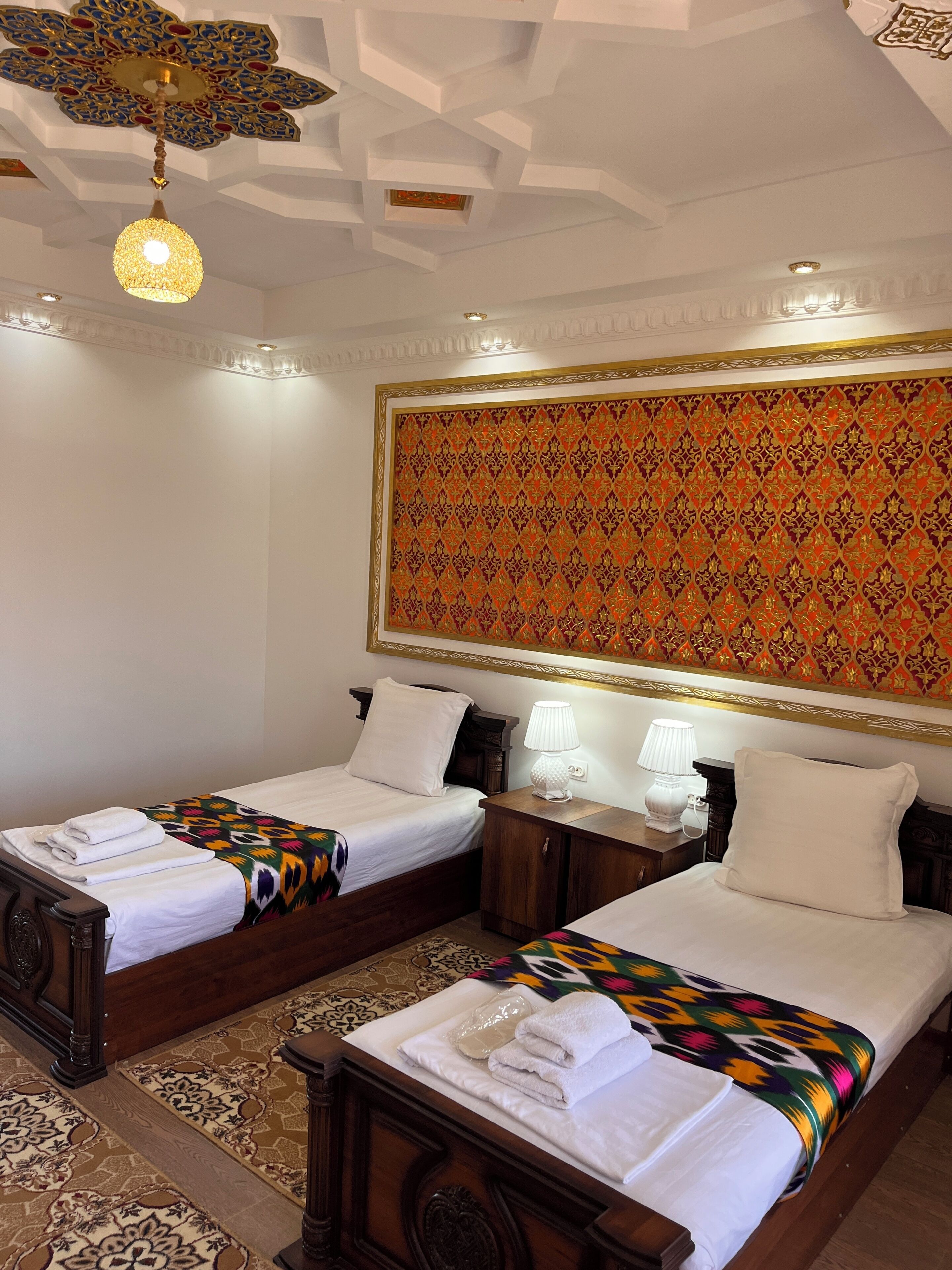 A hotel room with two beds, a decorative ceiling, and a patterned wall.