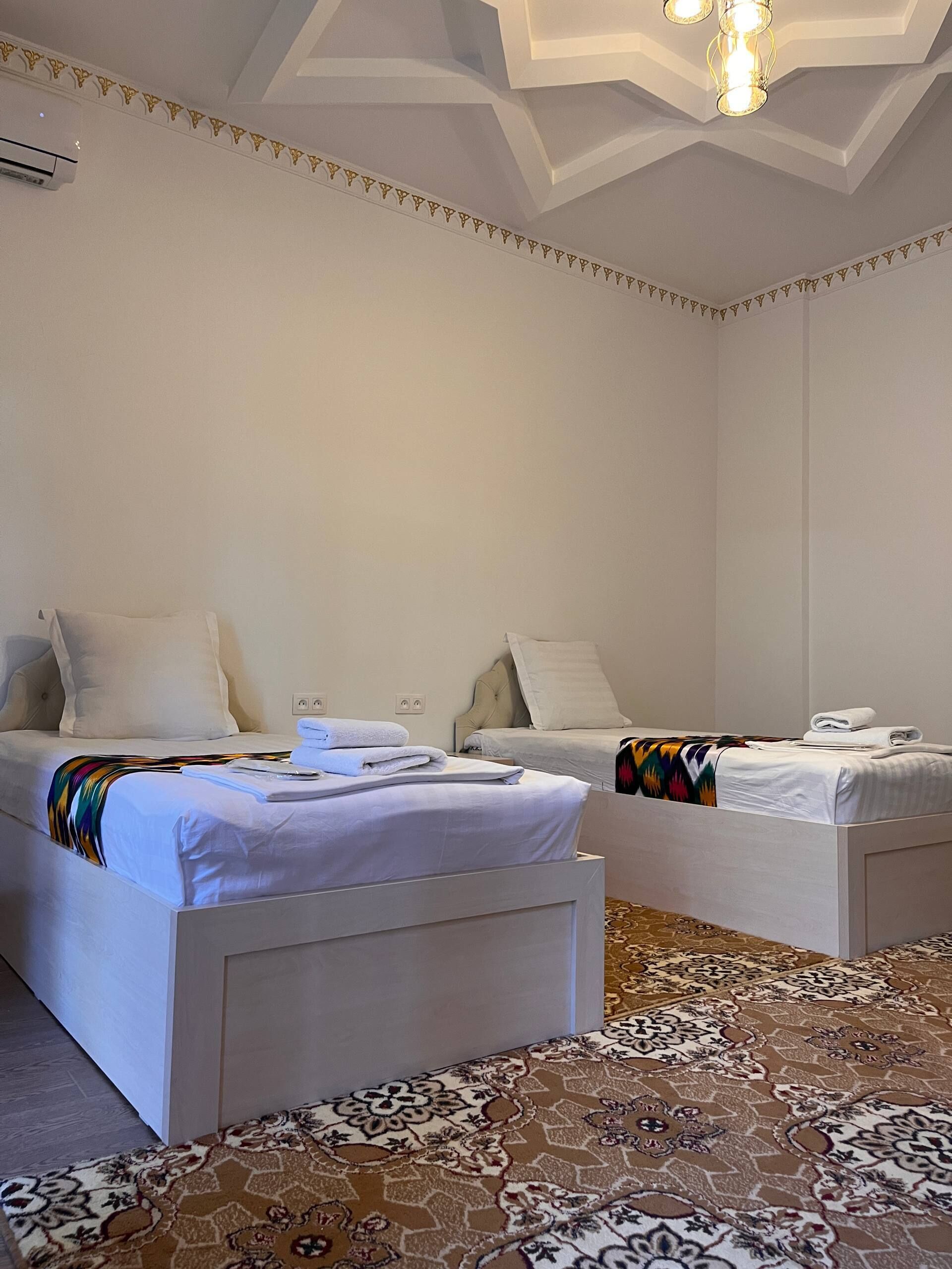 A hotel room with two beds, a patterned carpet, and a modern ceiling design.