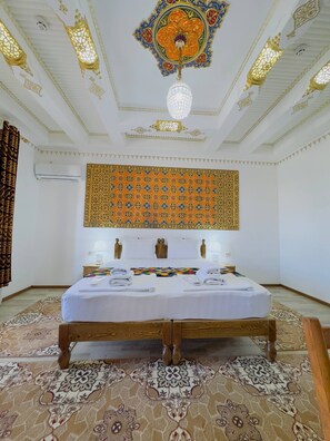 A hotel room with a large bed, a patterned wall hanging, and a chandelier. - LOLA Boutique Hotel (Bukhara)