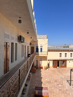 A building with a covered balcony, multiple doors, and a tiled courtyard. - LOLA Boutique Hotel (Bukhara)