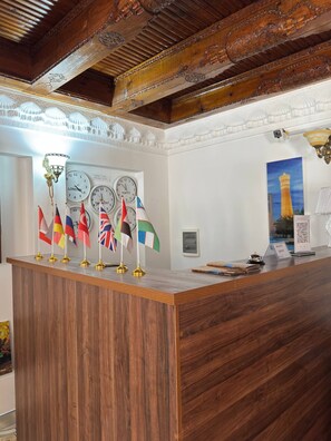 A reception desk with multiple clocks and flags, a framed picture of a tower, and a wooden ceiling. - LOLA Boutique Hotel (Bukhara)