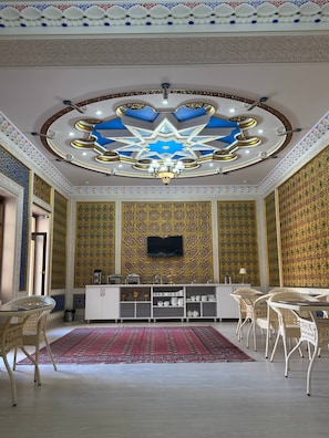 A room with a star-shaped ceiling, a flat-screen TV mounted on the wall, a white console table with various items, wicker chairs, and a patterned carpet. - LOLA Boutique Hotel (Bukhara)