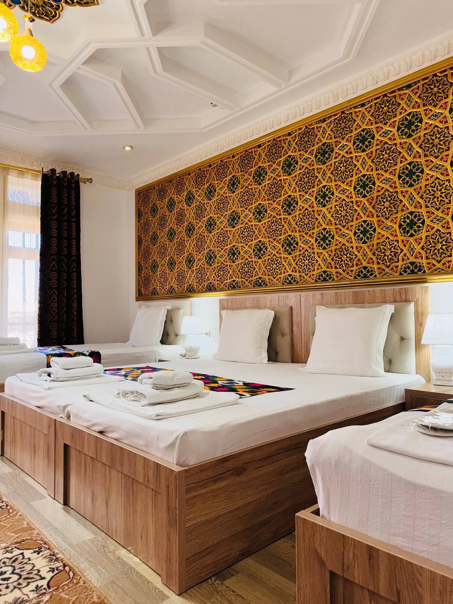 Una habitación de hotel con una cama grande, dos camas más pequeñas, un muro decorativo y suelo de madera.