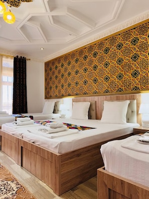 A hotel room with a large bed, two smaller beds, a decorative wall, and a wooden floor. - LOLA Boutique Hotel (Bukhara)