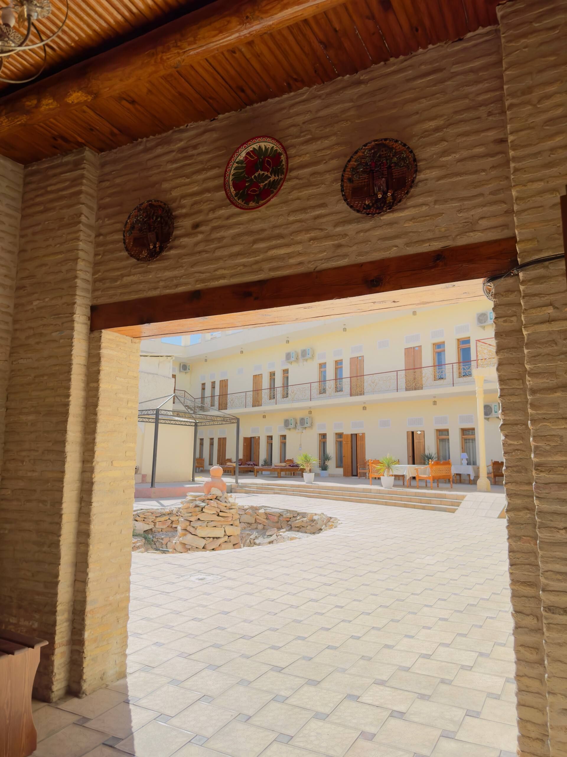 A courtyard with a stone fountain, a wooden bench, and a building with multiple windows and balconies.