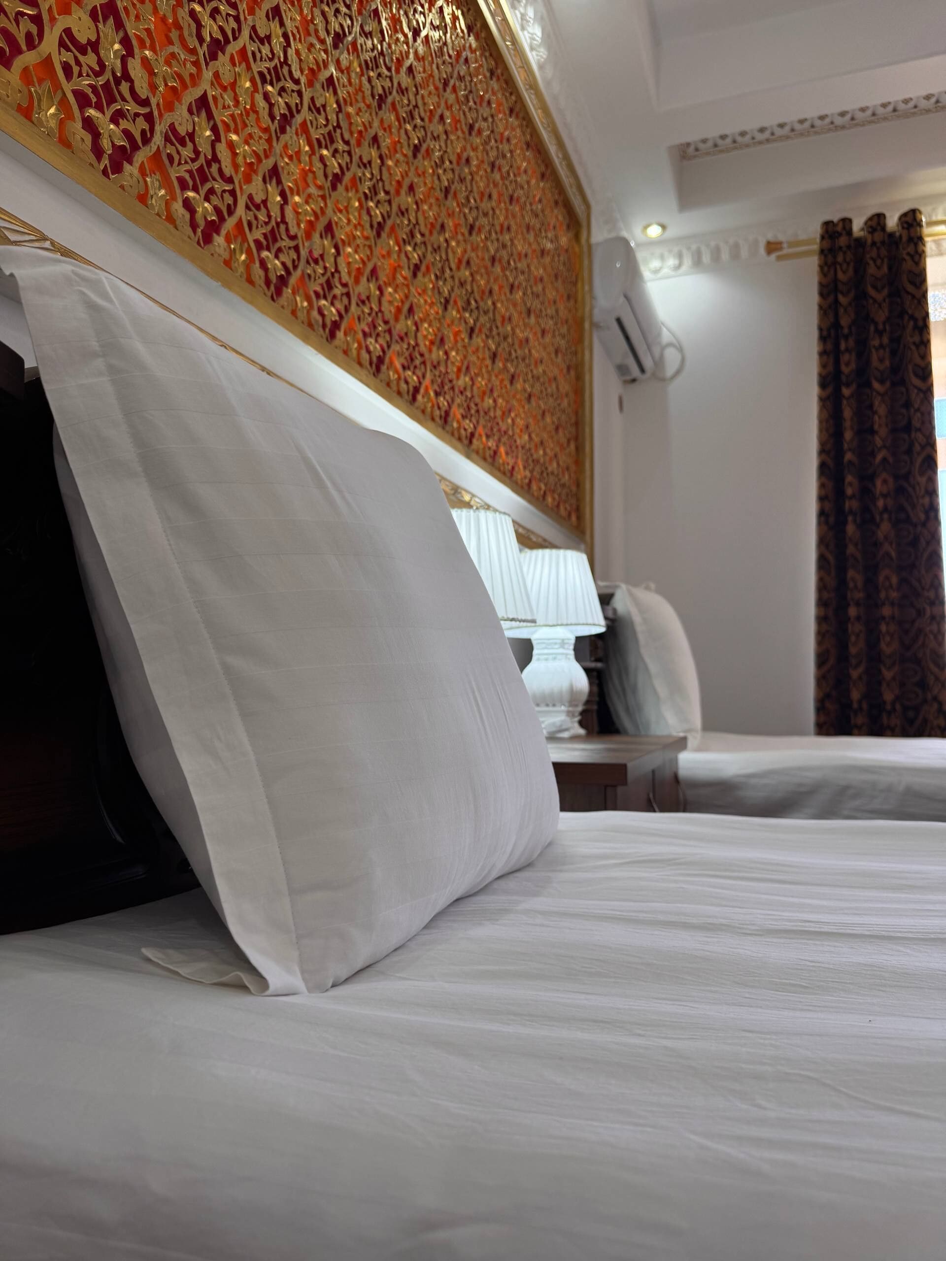 A hotel room with a large bed, a decorative wall, and a window with curtains.