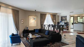 A modern living room with a black sofa, blue armchairs, and a coffee table. There is a dining area with a black table and chairs, and a kitchen visible in the background.