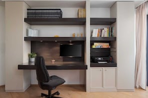 A modern home office setup with a desk, chair, shelves, and a television.
