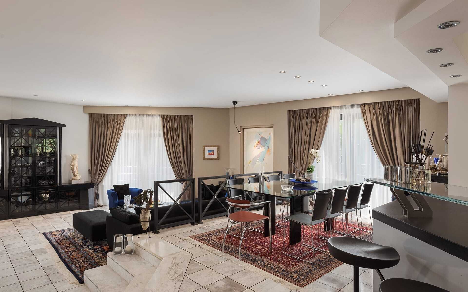 A modern dining area with a glass table, black chairs, and a red patterned rug.