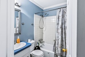 Et badeværelse med badekar, toilet, håndvask og bruseforhæng med et mønster.