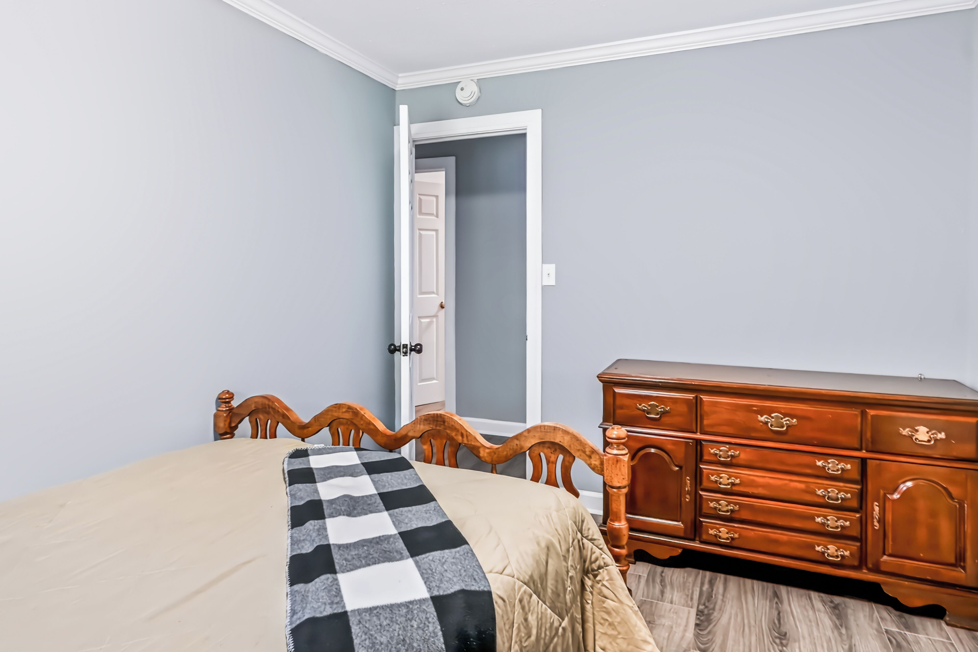 Een slaapkamer met een bed, een dressoir en een deur naar een andere kamer.