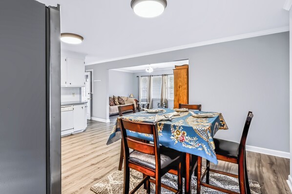 Un comedor con una mesa dispuesta para cuatro personas, sillas de madera y un mantel estampado.