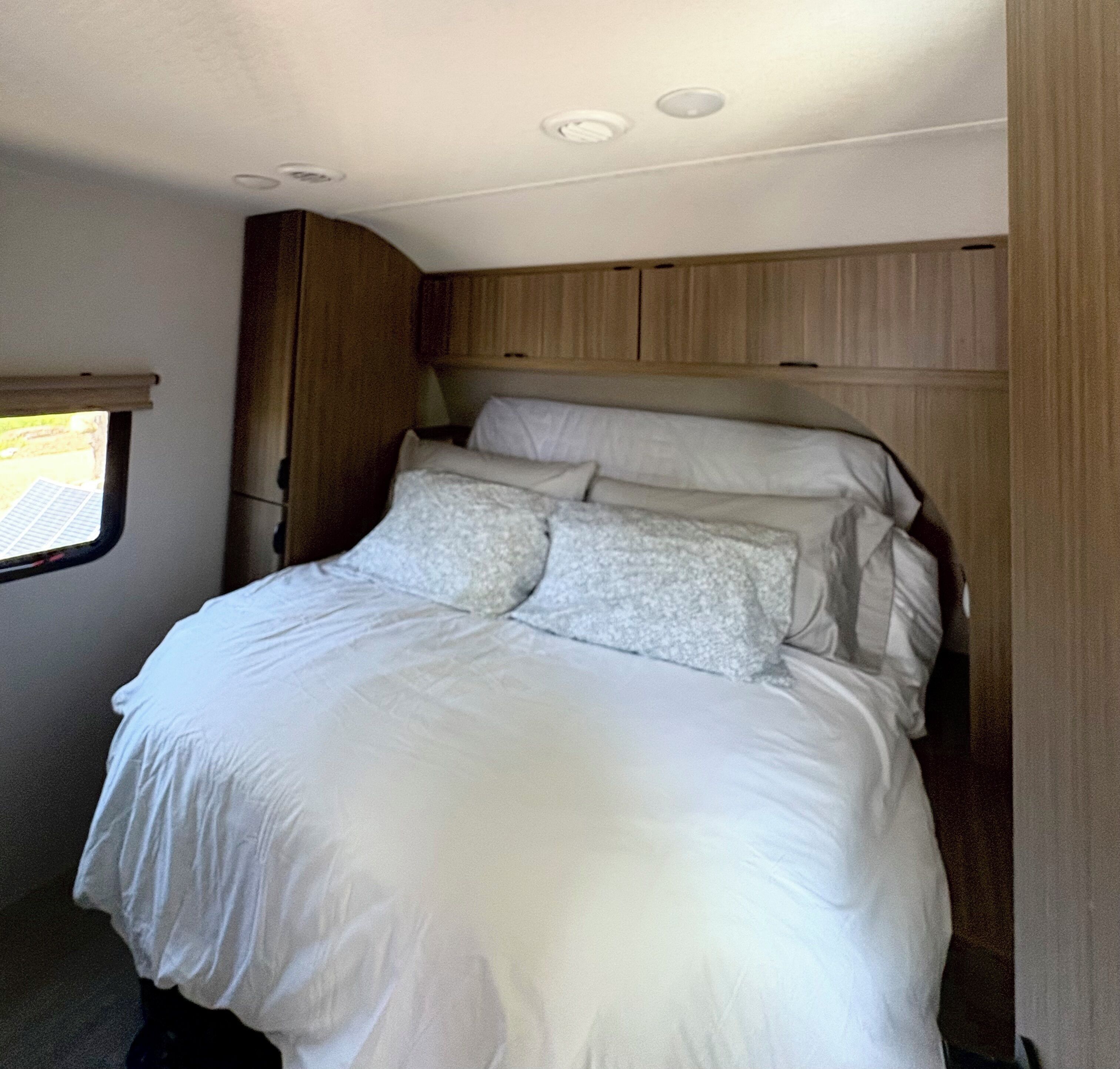 A bed with white linens in a room with wooden paneling and a window.
