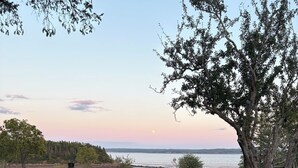 A gravel patio with a picnic table and red chairs, overlooking a body of water. - Private Bay of Fundy Escape | Ocean Views, Sauna & Tides (Upper Rockport)