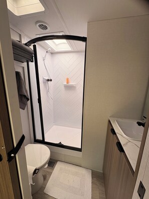 A compact bathroom with a shower enclosure, a toilet, and a sink. - Private Bay of Fundy Escape | Ocean Views, Sauna & Tides (Upper Rockport)