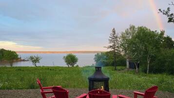 Eine Seenlandschaft mit Feuerstelle und roten Adirondack-Stühlen.