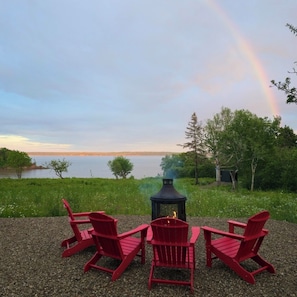 A lakeside setting with a fire pit and red Adirondack chairs. - Private Bay of Fundy Escape | Ocean Views, Sauna & Tides | RAW-Rest and Wander (Upper Rockport)