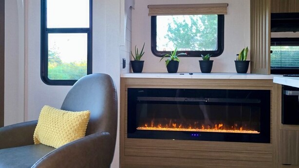 A modern living room with a fireplace, a comfortable leather chair, and a window with a view of greenery.