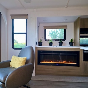 A modern living room with a fireplace, a comfortable leather chair, and a window with a view of greenery. - Private Bay of Fundy Escape | Ocean Views, Sauna & Tides | RAW-Rest and Wander (Upper Rockport)