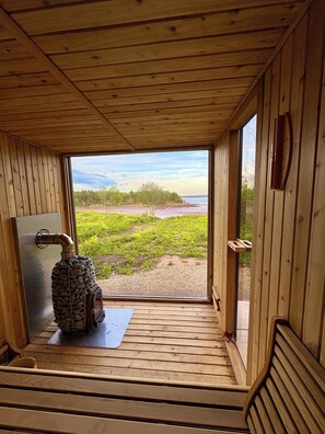A wooden cabin with a stone fireplace, a view of a beach, and a door leading outside.