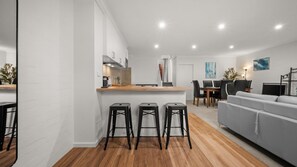 A modern kitchen with a central island, bar stools, a dining area with a table and chairs, and a living room with a sofa. - Chase & Chill  stay in Phillip! (Phillip)
