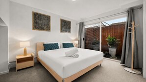 Ein Hotelzimmer mit Bett, Nachttisch, Lampe, Kunstwerk und Blick durch eine Schiebetür.