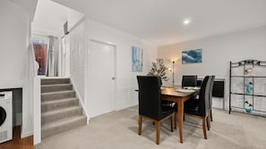 A dining area with a wooden table and black chairs, a staircase, and a white door. - Chase & Chill  stay in Phillip! (Phillip)