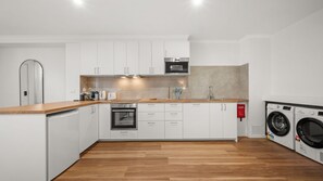 Eine moderne Küche mit weißen Schränken, einer Holzauskładung, einem eingebauten Backofen, einer Mikrowelle und einer Waschmaschine.