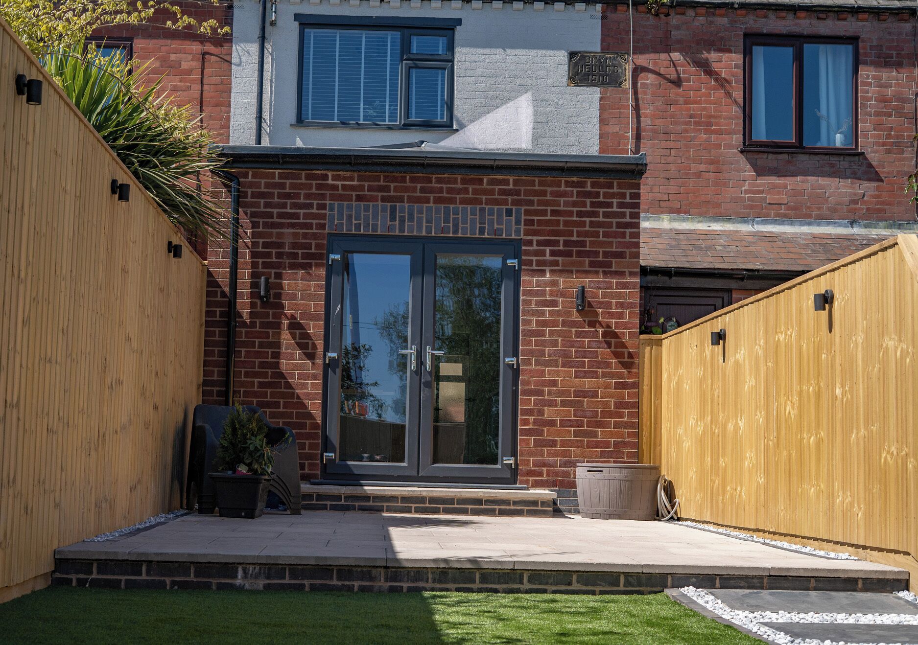 A residential building with a brick facade, a glass door entrance, and a wooden fence.