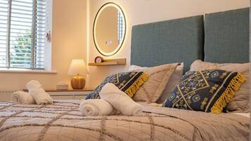 A neatly made bed with rolled towels, a bedside lamp, and a wall-mounted mirror.