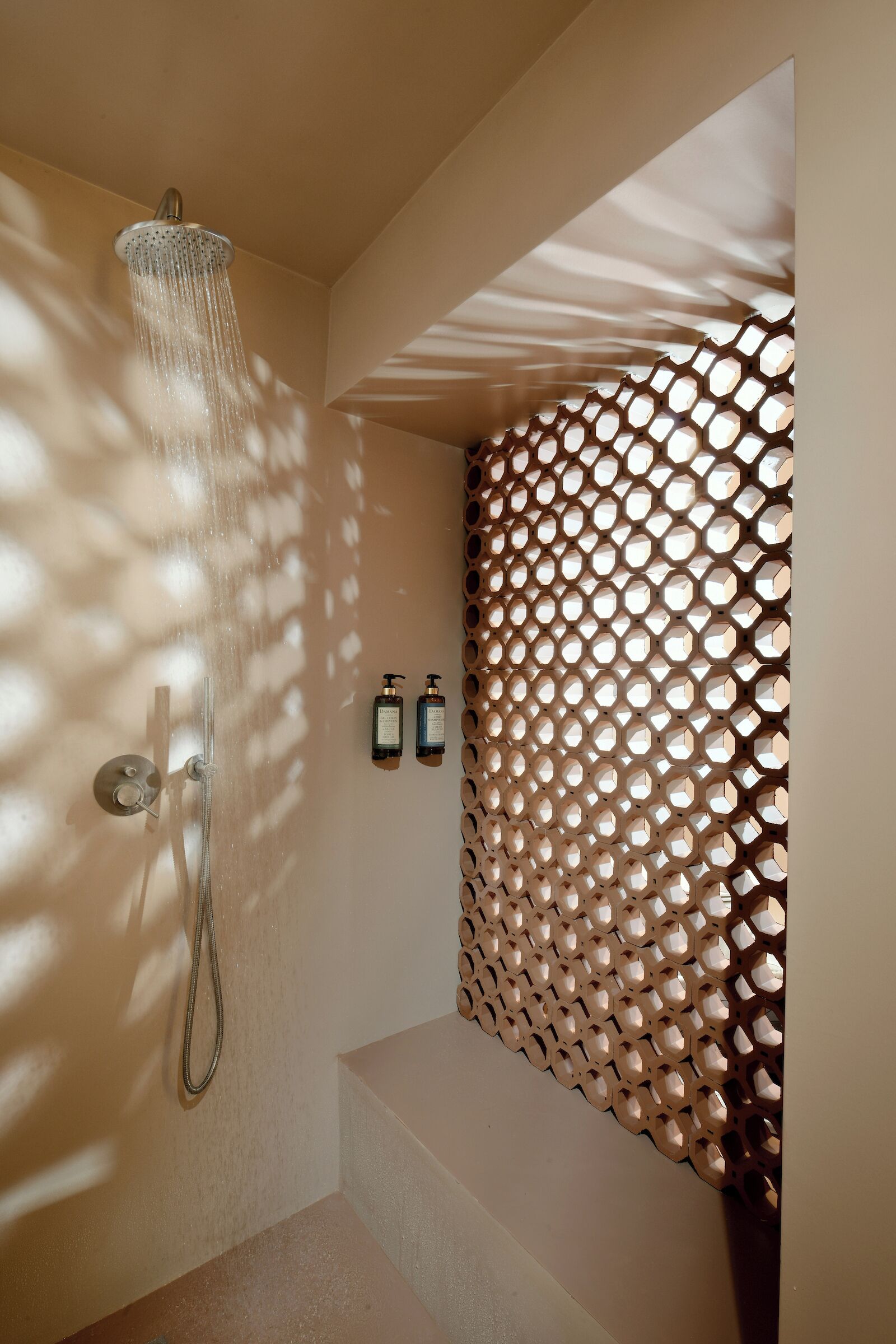 Une douche équipée d’un pommeau de douche à effet pluie, d’un distributeur de savon mural et d’un mur orné d’un motif géométrique.