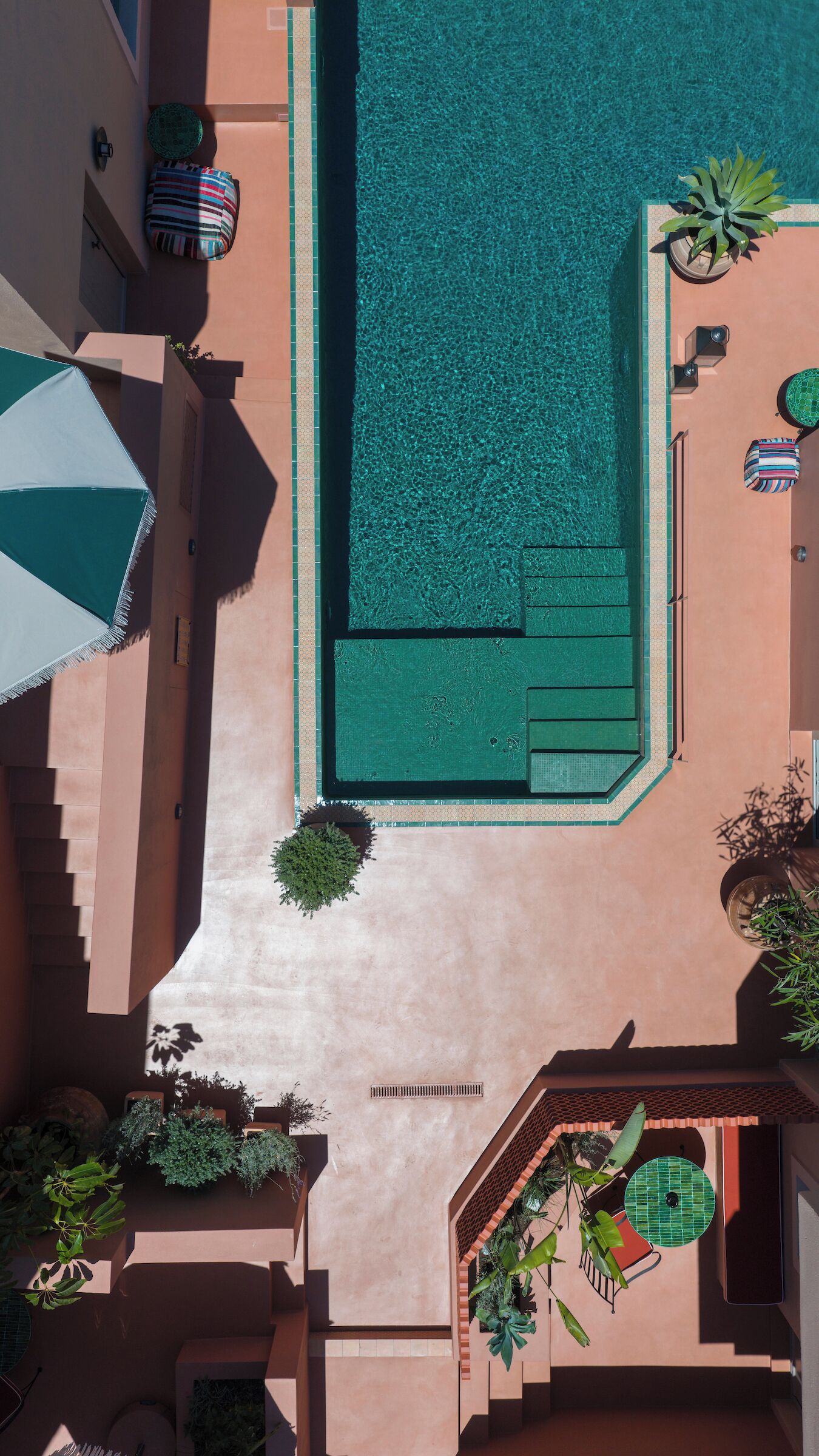 An aerial view of a swimming pool with a tiled deck, lounge chairs, and potted plants.