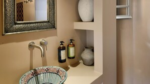 A bathroom with a decorative mirror, a bowl sink, and shelves with toiletries. - Terra Verde Oia Suites - Cotto Standard Room (Oia)