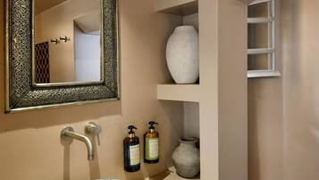 A bathroom with a decorative mirror, a bowl sink, and shelves with toiletries.
