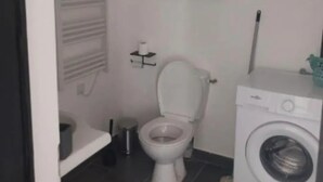 Ein kleines, kompaktes Badezimmer mit Toilette, Waschmaschine und einem Schrank über der Toilette.