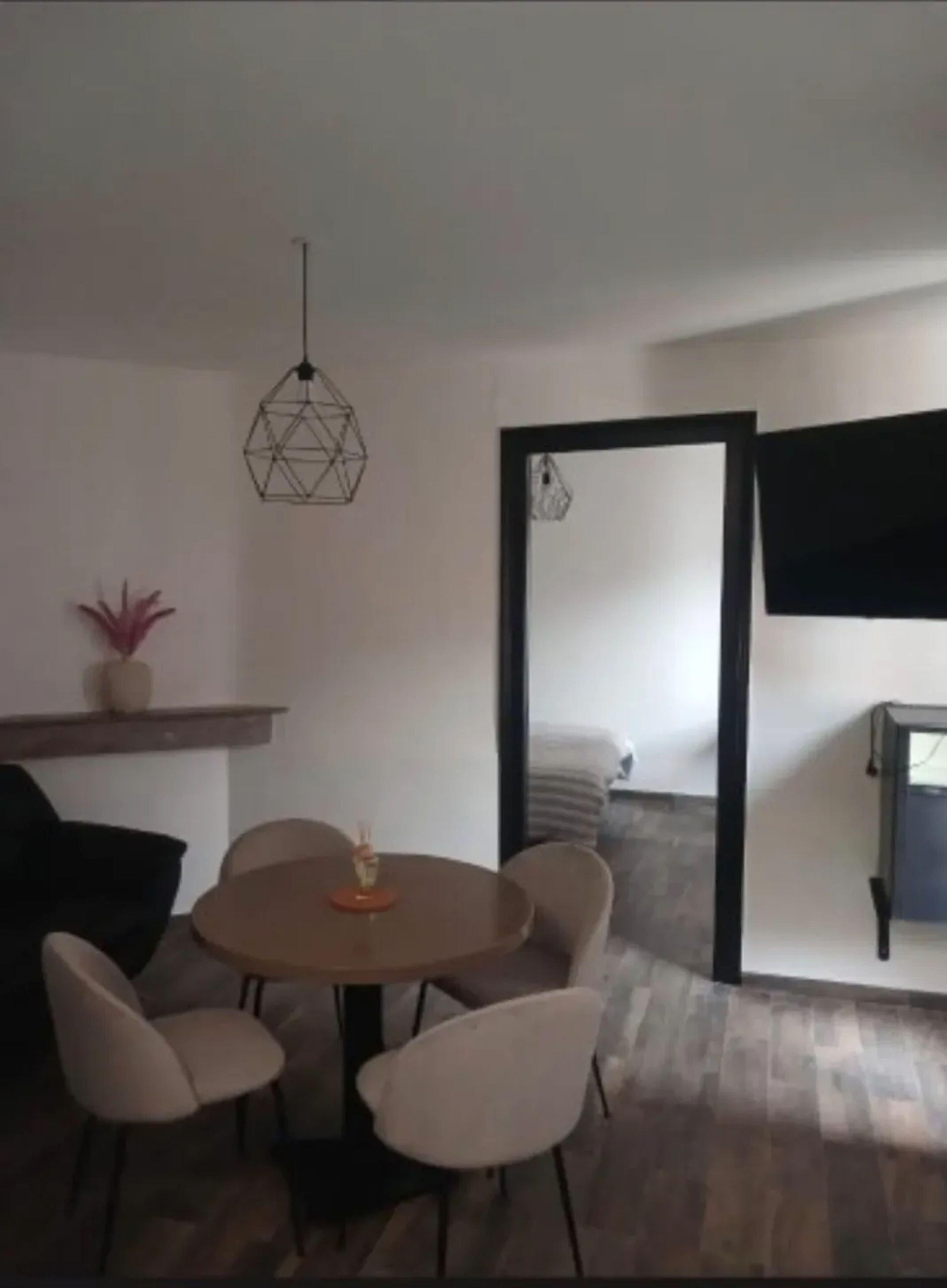 Ein Essbereich mit einem runden Tisch, vier Stühlen, einer hängenden Leuchte und einem durch einen offenen Durchgang erkennbaren Bett.