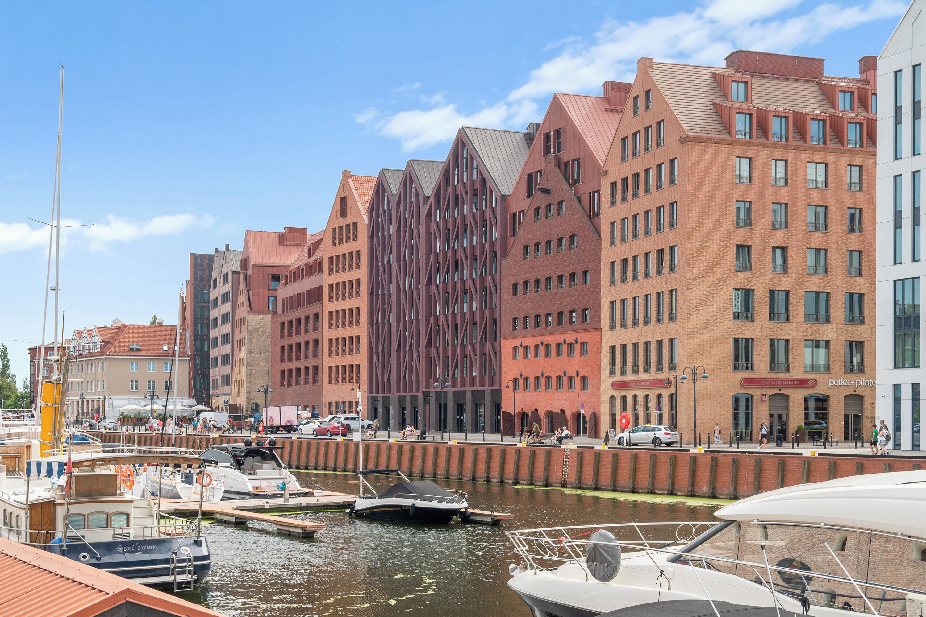 A waterfront cityscape with modern buildings, a marina with boats, and a clear sky.