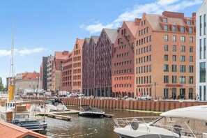 A waterfront cityscape with modern buildings, a marina with boats, and a clear sky. - Granaria Premium with Jacuzzi and Patio (Gdańsk)