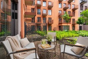 A courtyard with outdoor seating, a small table with drinks, and a view of a multi-story building with balconies. - Granaria Premium with Jacuzzi and Patio (Gdańsk)