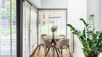 A modern interior with a round table and chairs, large windows with blinds, and a potted plant.