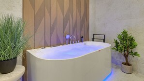 Ein modernes Badezimmer mit einer freistehenden Badewanne, einer Wandverkleidung aus Holz und zwei Topfpflanzen.