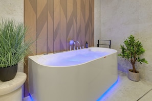Ein modernes Badezimmer mit einer freistehenden Badewanne, einer Wandverkleidung aus Holz und zwei Topfpflanzen.