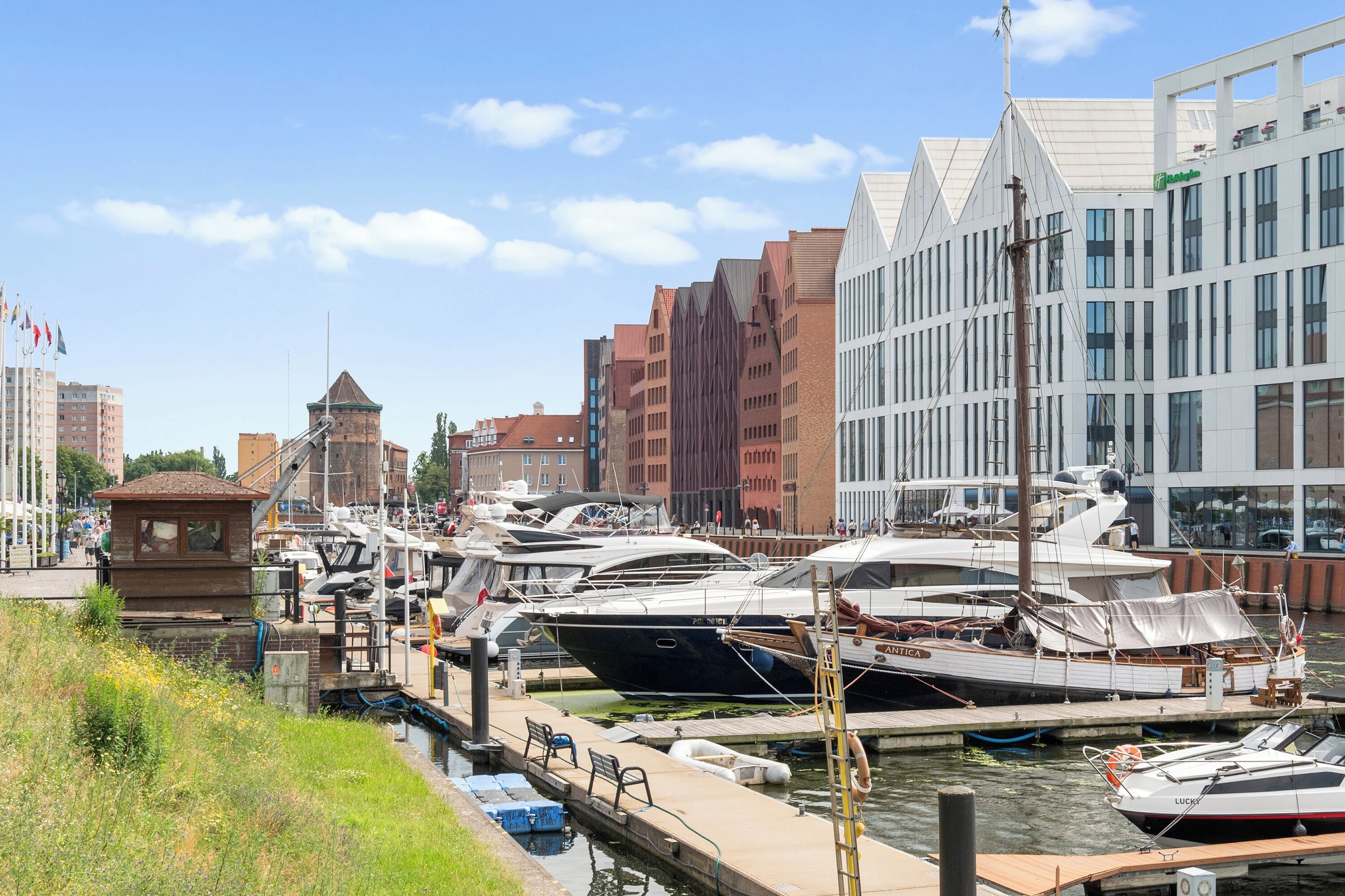 A marina with boats docked, a tower, and modern buildings in the background.
