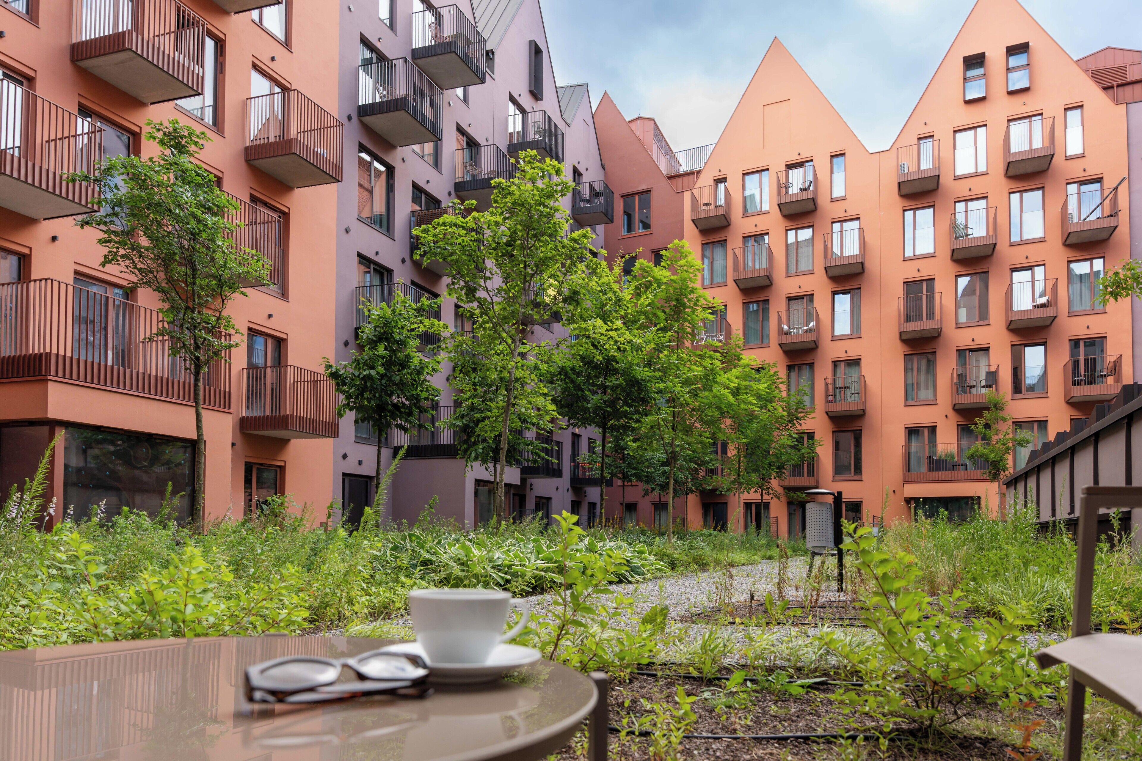 Ein Innenhof mit modernen Wohngebäuden, einem Tisch mit Tasse und Untertasse sowie einem Stuhl.