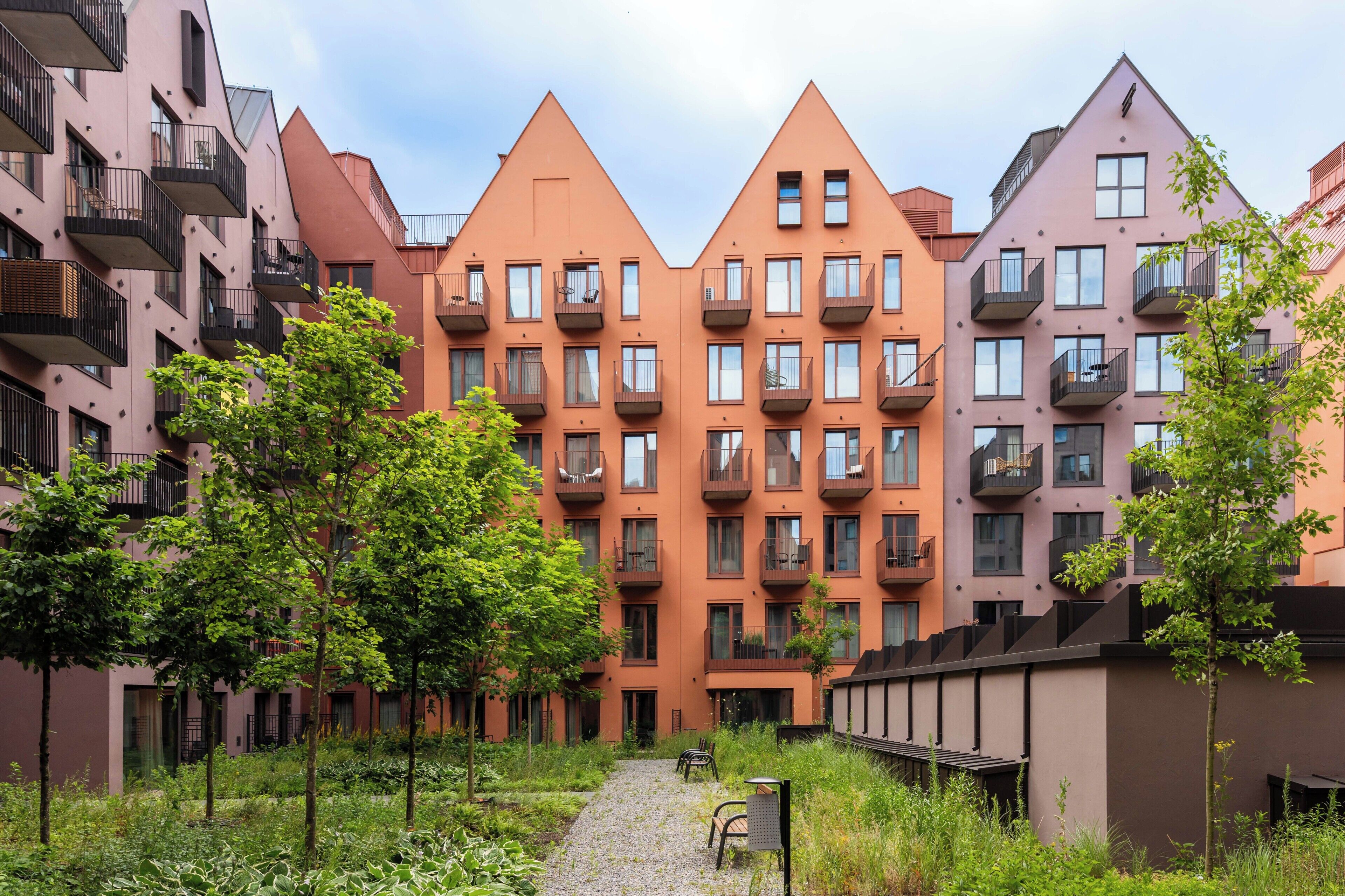 Eine Reihe moderner Apartmenthäuser mit Balkonen, einem zentralen Weg und umliegender Grünfläche.