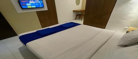 A hotel room with a bed, a TV mounted on the wall, and a desk with a chair.