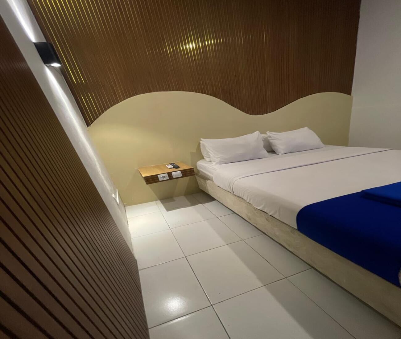 A hotel room with a bed, a nightstand, and a wall-mounted shelf.