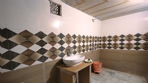 Un baño con un lavamanos blanco, un taburete pequeño y una pared de azulejos con un diseño geométrico.