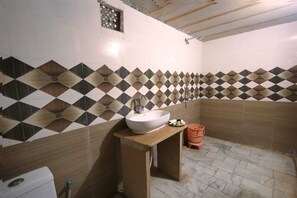 A bathroom with a white sink, a small stool, and a tiled wall with a geometric pattern. - The Sandy Resort  (Sam)